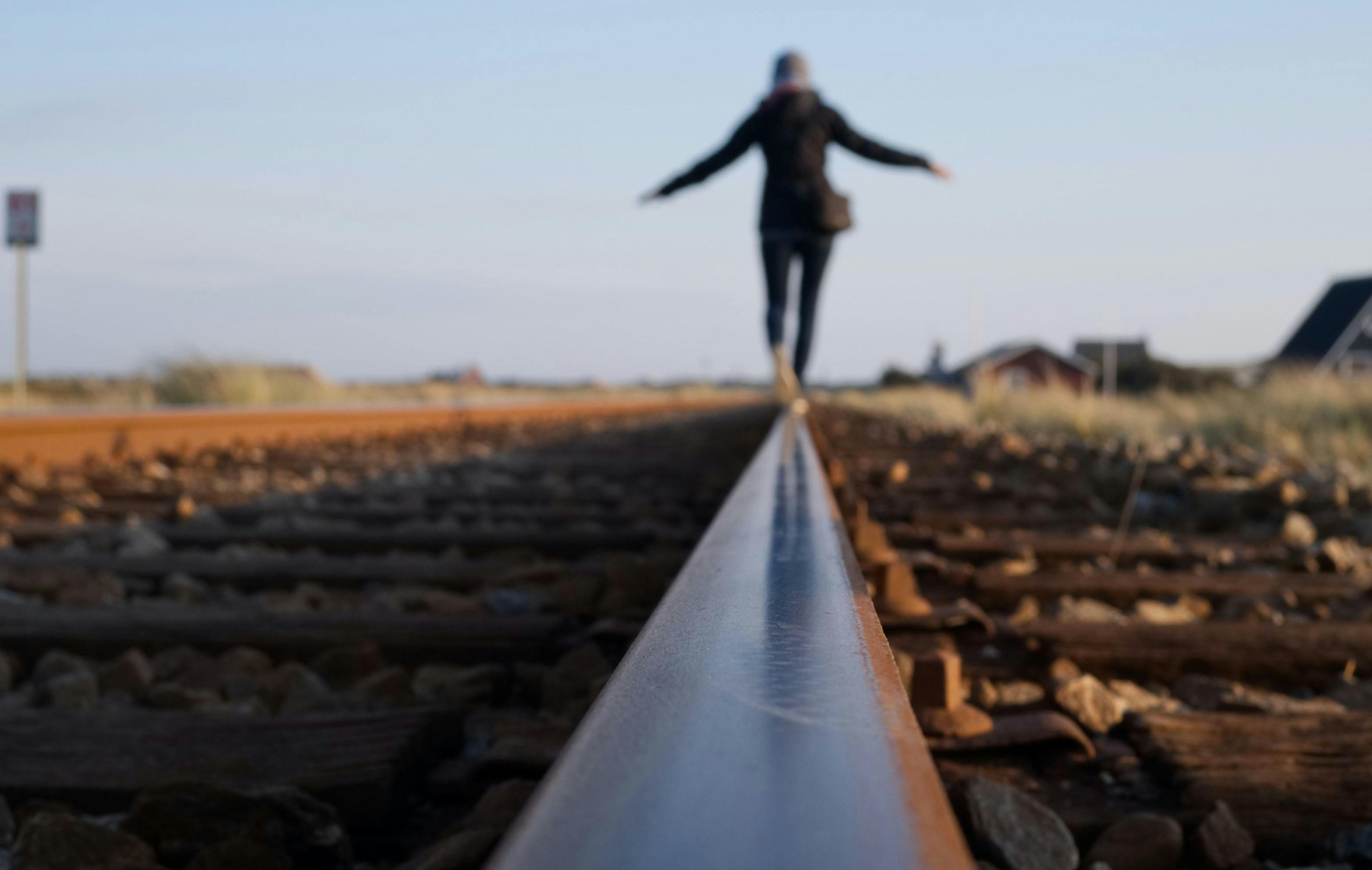 Woman balancing on a train track rail on a clear day